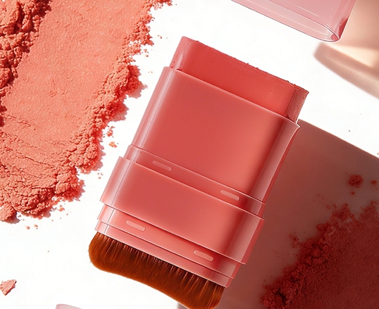 Top‑down shot of coral retractable blush brush container scattered with loose blush powder on white surface